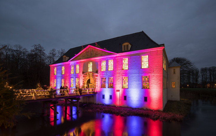 Beleuchtetes Barockschloss Dornum bei Abenddämmerung auf einem Weihnachtsmarkt im Winter.
