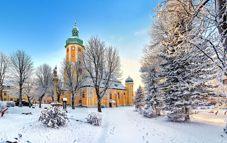 Kirche St. Laurentius in Horní Blatná im Winter, umgeben von verschneiten Bäumen