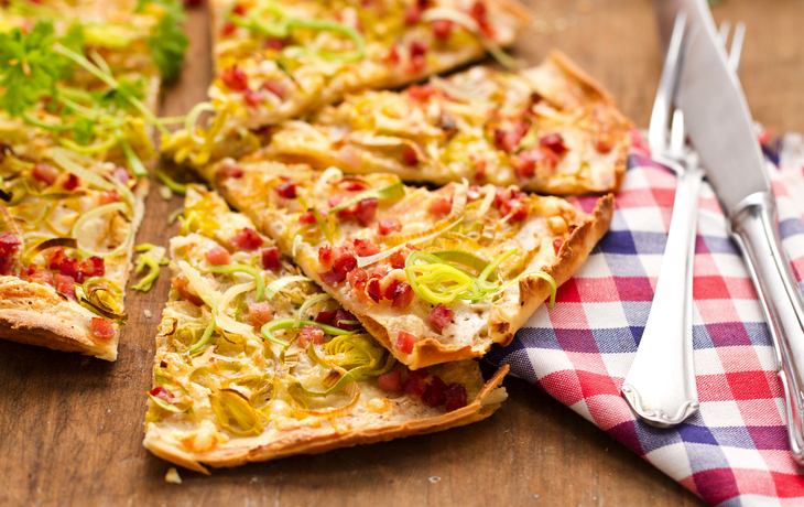 Flammkuchen mit Lauch und Schinkenwürfeln auf Holztisch