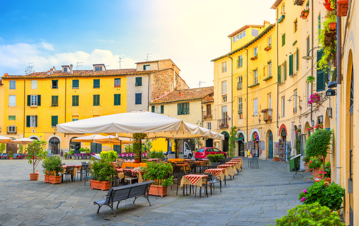 Piazza mit Cafés und Restaurants in Lucca, Italien, umgeben von bunten Häusern.