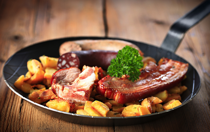 Schlachtplatte mit verschiedenen Würsten und Bratkartoffeln in einer Pfanne.
