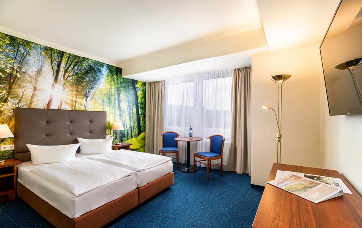 Helles Hotelzimmer mit Doppelbett, Sesseln und Waldtapete.