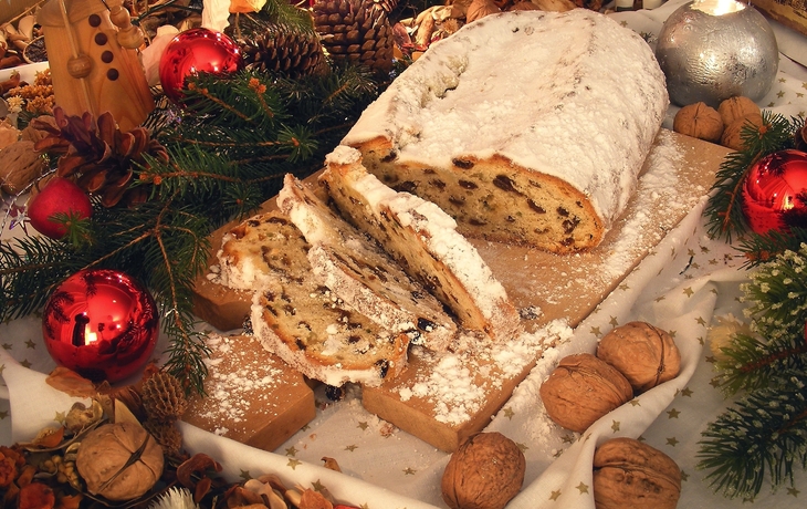 Traditioneller Weihnachtsstollen mit Nüssen und Weihnachtsdekoration auf Holztisch.