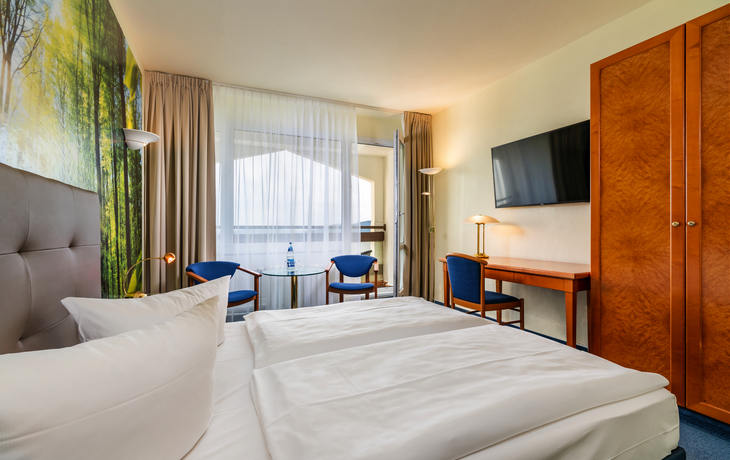 Zimmer im AHORN Berghotel Friedrichroda mit Doppelbett und Sitzgelegenheit.