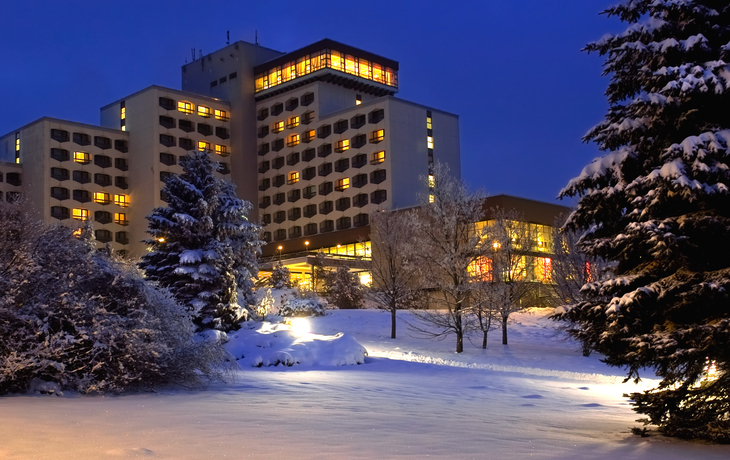 Hotel im Winter mit verschneiten Bäumen, beleuchtete Fenster am Abend.