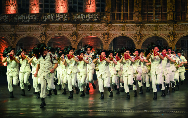 Musikkapelle in weißen Uniformen marschiert in einer festlichen Paradehalle.