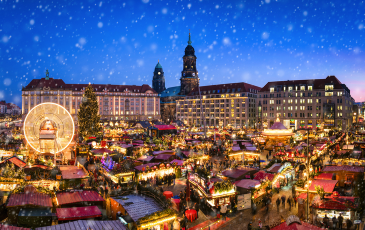 Striezelmarkt in Dresden bei Nacht mit Lichtern, Weihnachtsbaum und Karussell im Schnee.