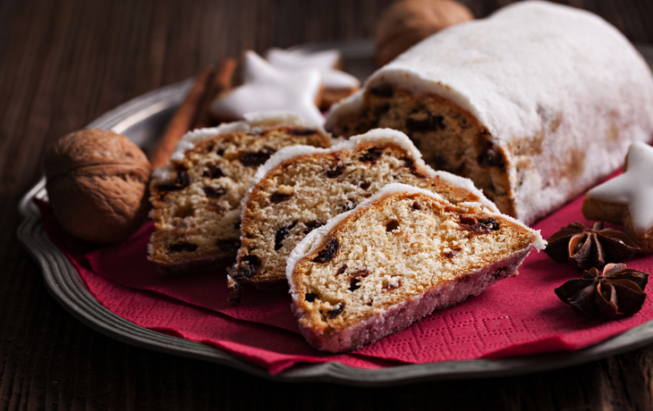 Christstollen auf einem Teller mit Zimtstangen und Sternanis auf Holztisch.