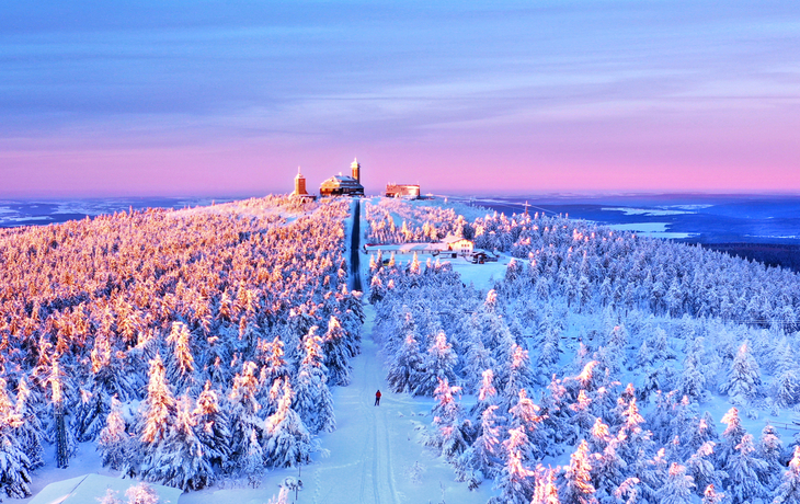 Verschneiter Fichtelberg bei Sonnenuntergang im Winter, mit Blick auf Skifahrer.
