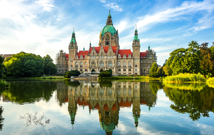 Neues Rathaus Hannover spiegelt sich im Wasser, umgeben von Natur.