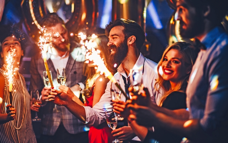 Menschen feiern Silvester mit Wunderkerzen und Sekt in festlicher Stimmung.