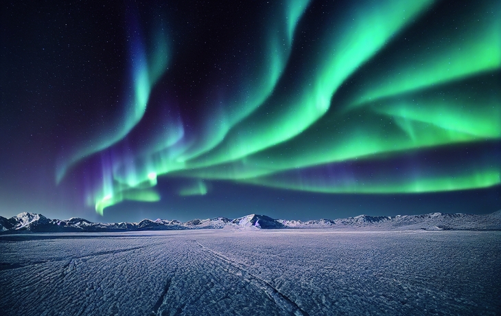 Polarlichter über verschneiter Landschaft in Norwegen bei Nacht.