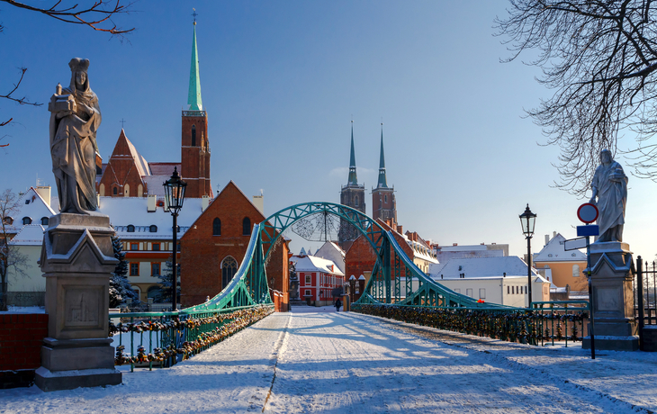 Dombrücke in Breslau im Winter mit Schnee und Kirchen im Hintergrund.