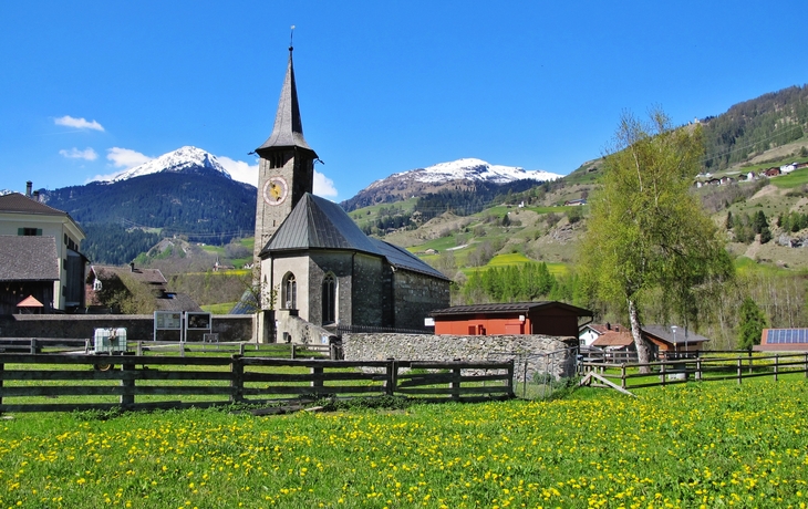 Kirche St. Martin in Zillis vor Bergkulisse und blauen Himmel.