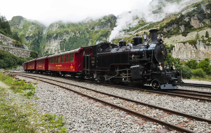 Historische Dampflokomotive zieht Zug durch Berglandschaft am Furkapass.