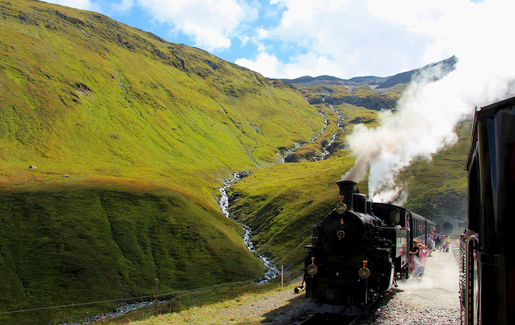 Dampfzug fährt durch grüne Berglandschaft am Furkapass.