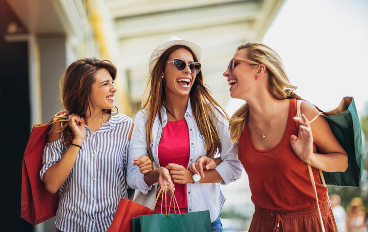 Drei Frauen mit Einkaufstaschen lachen bei einem Stadtbummel.