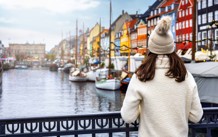 Frau im Wintermantel blickt auf den Nyhavn-Hafen in Kopenhagen