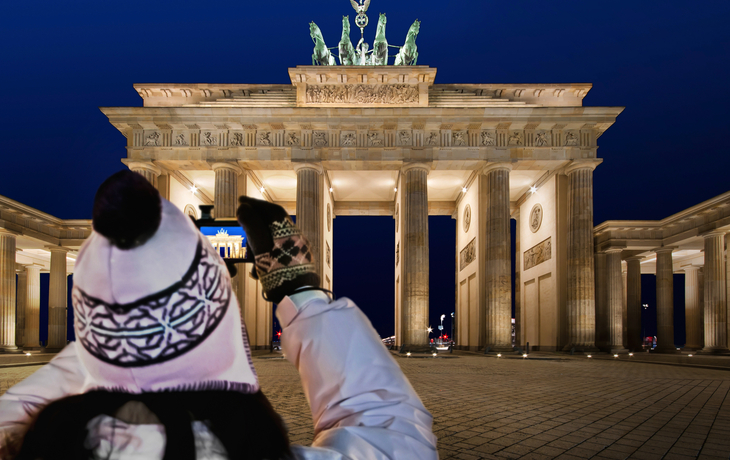 Touristin fotografiert das beleuchtete Brandenburger Tor bei Nacht im Winter.