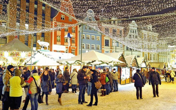 Verschneiter Weihnachtsmarkt in der Rostocker Altstadt mit Ständen und Lichtern.
