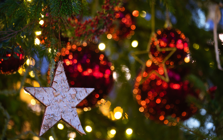 Christbaumkugeln und Stern als Weihnachtsschmuck an einem Baum mit Lichtern.