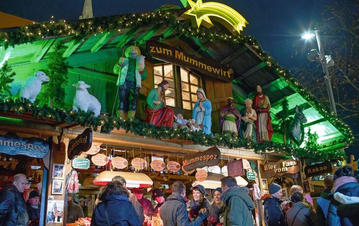 Besucher auf einem weihnachtlich beleuchteten Weihnachtsmarkt mit Krippe und Holzhütte in Braunschweig.