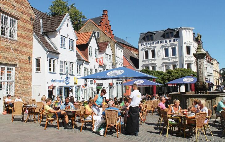 Straßencafé voller Menschen am Nordermarkt in Flensburgs Altstadt bei sonnigem Wetter.