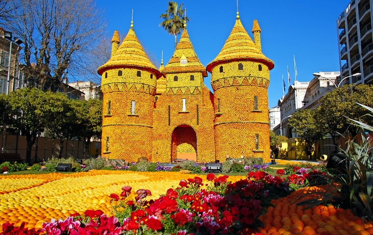 Große Zitronenskulptur als Schloss beim Zitronenfest in Menton, umgeben von Blumen.
