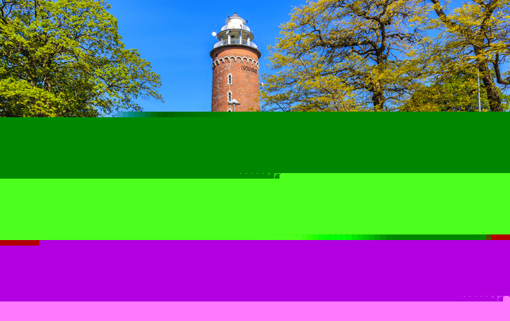 Leuchtturm von Kołobrzeg an der Ostsee, umgeben von Bäumen und einem Weg.