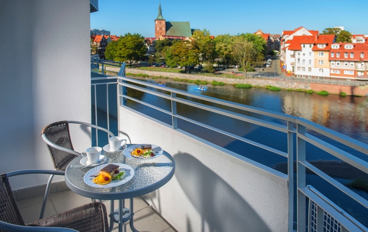 Blick von einem Balkon auf einen Fluss und eine Kirche im Hintergrund.