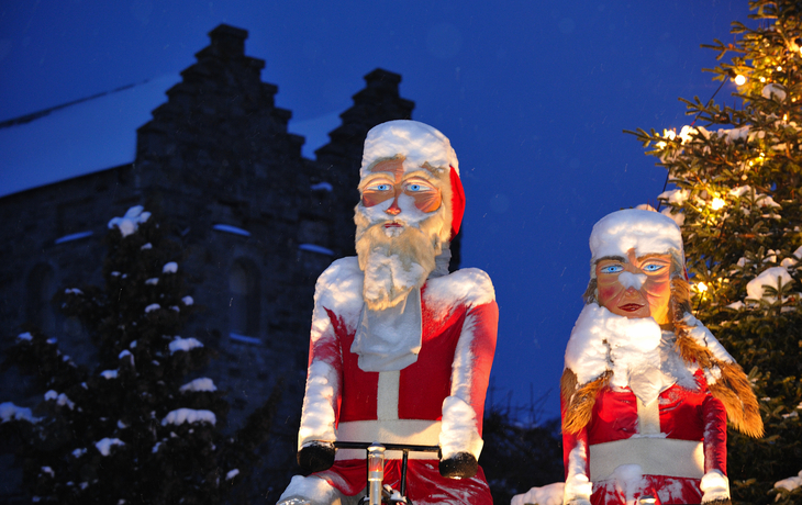 Zwei weihnachtlich bekleidete Elfenfiguren im Schnee vor einem Gebäude.