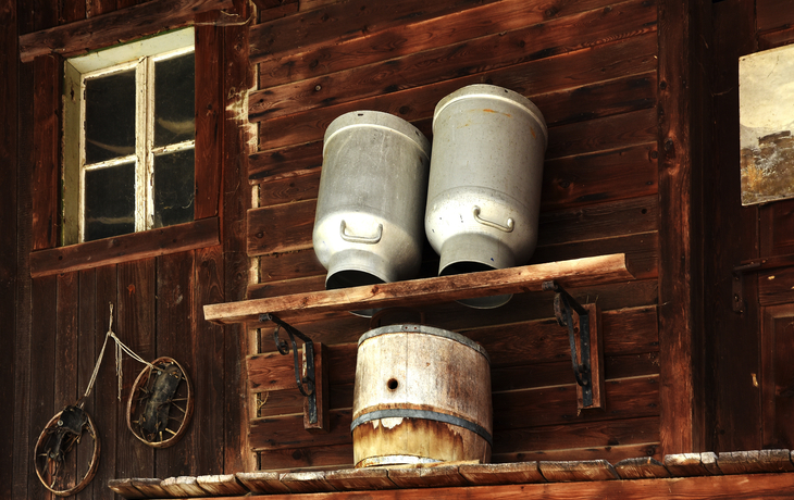 Zwei Milchkannen und ein Fass auf einem rustikalen Holzregal.