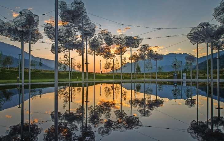 Kunstinstallation mit gespannter Drahtskulptur über einem Wasserbecken bei Sonnenuntergang.