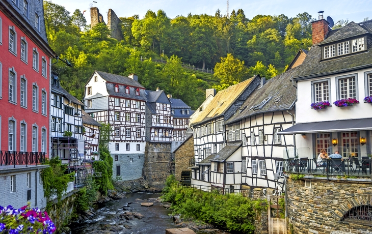 Fachwerkhäuser in Monschau mit Kopfsteinpflaster und fließendem Bach.