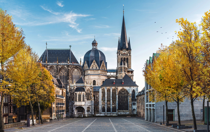 Aachener Dom im Herbst mit gelben Laubbäumen im Vordergrund