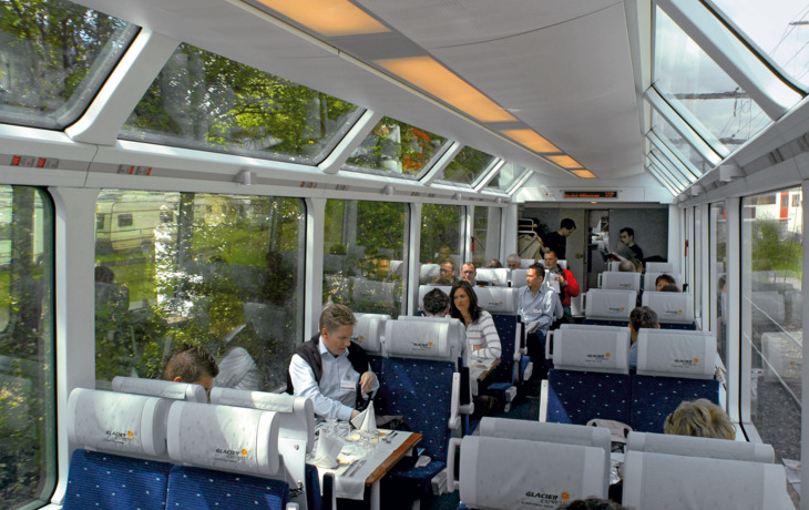 Blick in einen Panorama-Wagen des Glacier-Express mit Passagieren und schöner Aussicht.