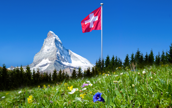 Matterhorn bei Sonnenschein mit Schweizer Flagge und einer Blumenwiese im Vordergrund