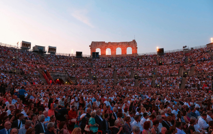 Menschenmenge in antikem Amphitheater bei Sonnenuntergang.