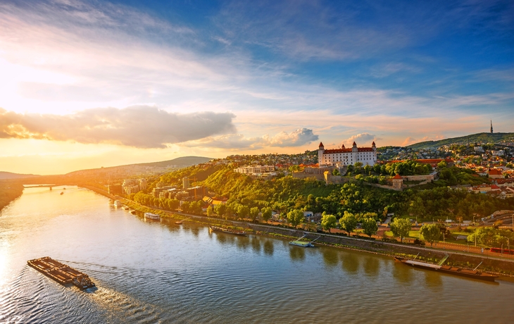 Blick auf Bratislava mit Burg und Donau bei Sonnenuntergang.