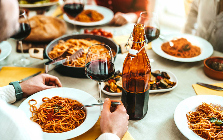 Gruppe von Freunden, die in einem italienischen Restaurant Spaghetti und Rotwein genießen.