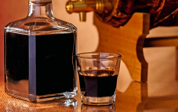Flasche und Glas mit Balsamico vor hölzernem Fass.