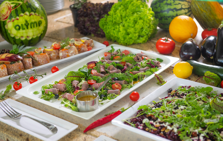 Verschiedene Speisen auf einem Buffet mit Gemüse und Obst dekoriert.