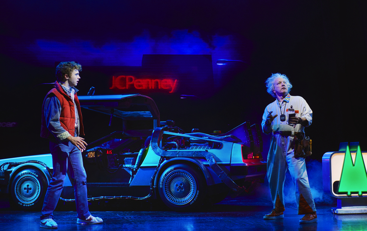 Eine Bühnenszene mit Marty McFly und Doc Brown vor einem DeLorean.