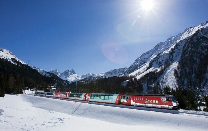 Der Glacier Express fährt durch schneebedeckte Berglandschaft bei Sonnenschein.