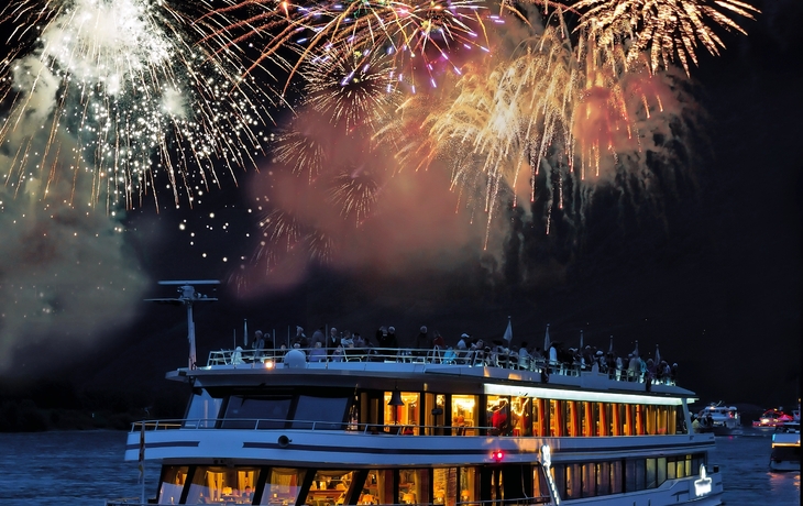 Feuerwerk über dem Rhein bei Rüdesheim mit beleuchtetem Schiff im Vordergrund.