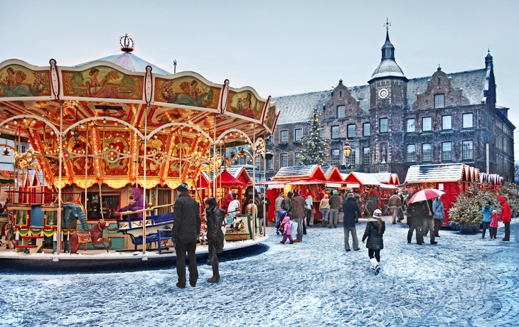 Weihnachtsmarkt in der Düsseldorfer Altstadt mit Karussell und Marktständen im Schnee.