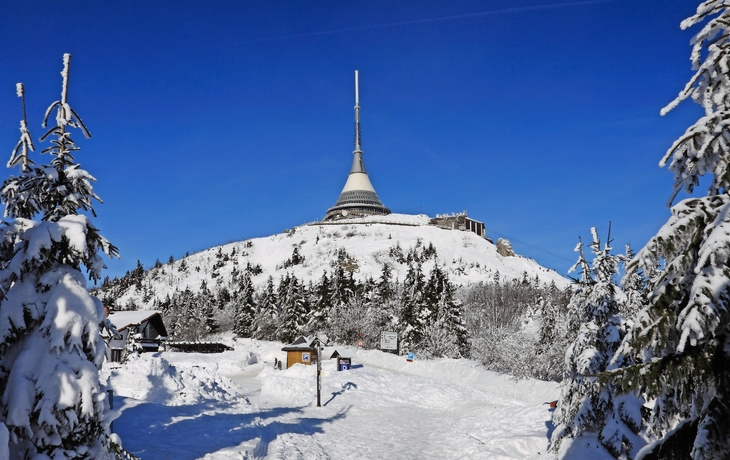 Schneebedeckter Berg mit einem futuristischen Turm vor blauem Himmel.