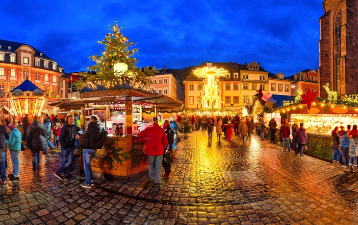 Weihnachtsmarkt am Abend mit erleuchteten Ständen und Menschen auf einem Kopfsteinpflaster.