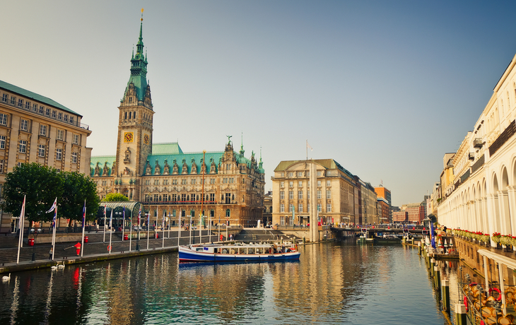 Hamburger Rathaus mit Wasserkanal und Boot im Vordergrund bei Sonnenschein.