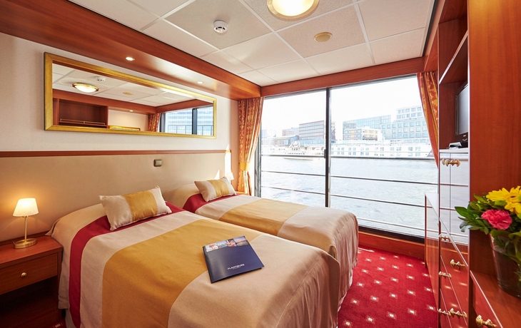 Kabine mit zwei Betten, großem Fenster und Ausblick auf Wasser und Stadt.
